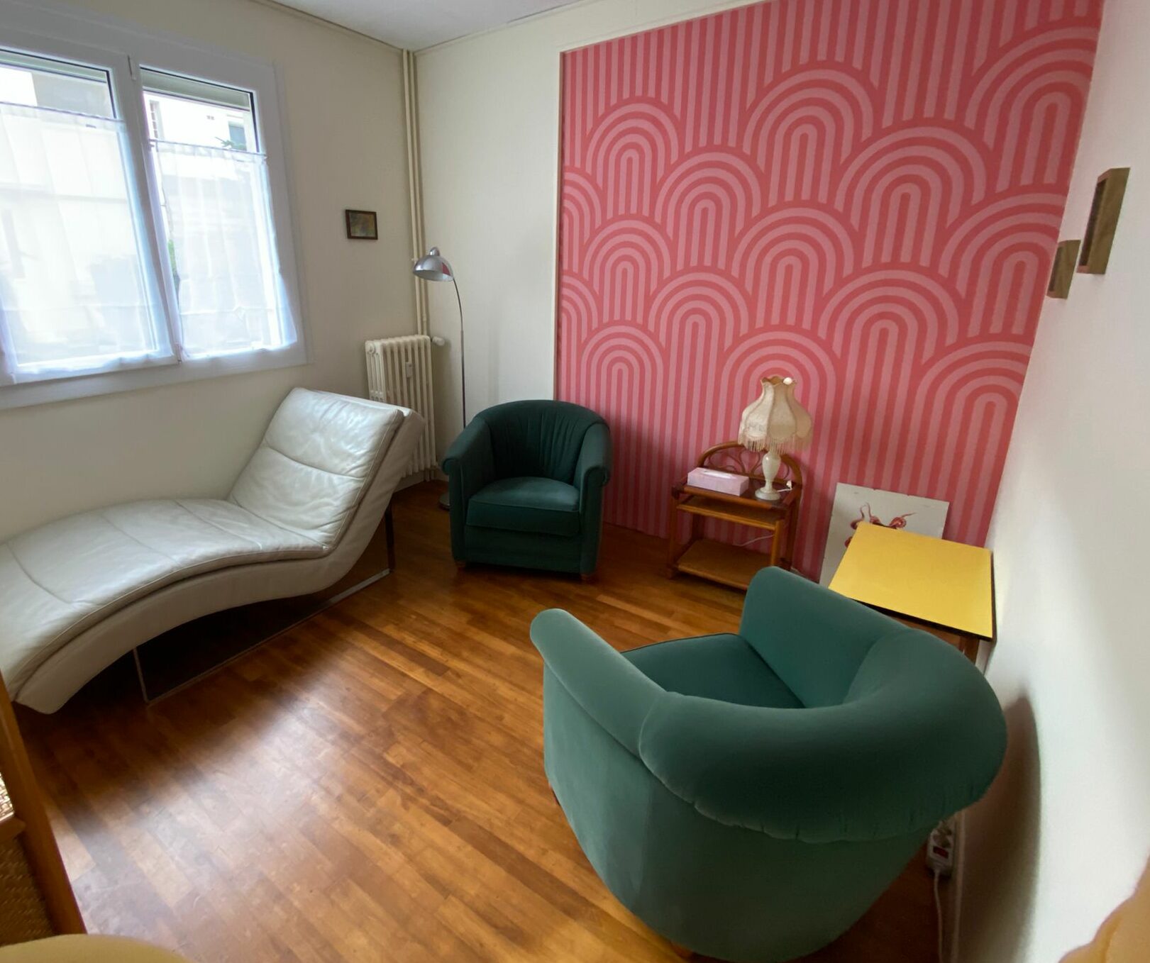 photo du cabinet dans lequel je consulte : 2 fauteuils club verts et un divan beige en cuir, une table basse jaune, du parquet au sol et une fenêtre au-dessus du divan